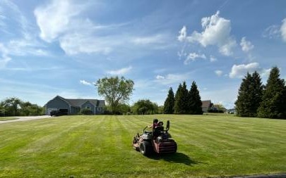A person riding a lawn mower in a large grassy field.